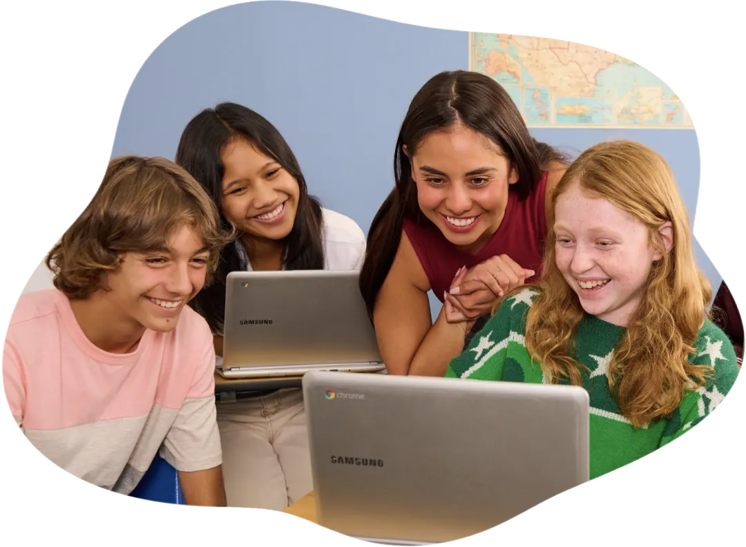 A teacher engages with a young group of cheerful students working on their laptops